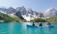 Three canoers paddling on a clear blue glacier lake framed by snow-capped mountains