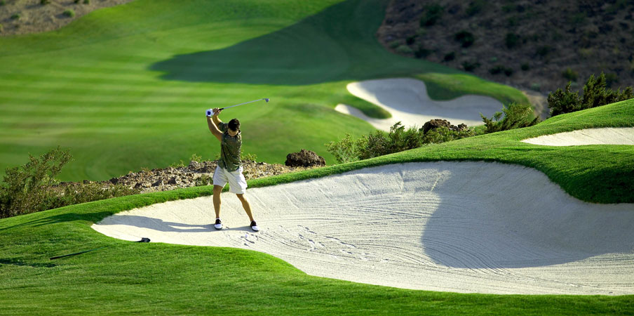 Man trying to hit out of a sand trap on a lush green golf course